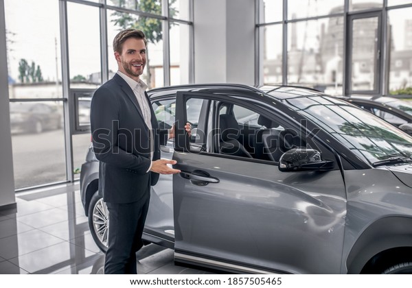 Auto dealership. Brown-haired male opening car\
door in showroom