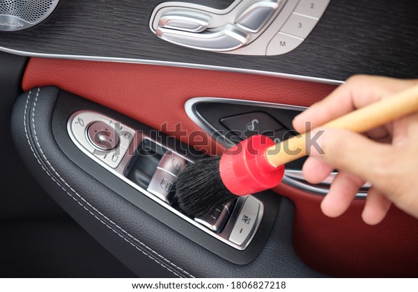 Auto detailer using detailing brush for\
cleaning dust in car window switch. Male hand cleaning car interior\
& upholstery with detail brush. Focus on brush. Car detailing\
concept. Car wash\
background.