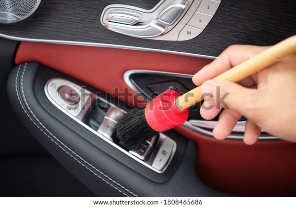 Auto detailer using detailing brush for
cleaning dust in the air vent. Male hand cleaning car interior
& upholstery with detail brush. Focus on brush. Car detailing
concept. Car wash
background.