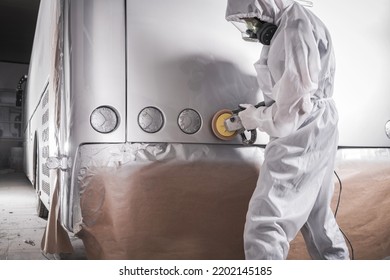 Auto Detailing Workshop Worker In Protective Suit And Mask Polishing Freshly Painted Varnish On A Motor Coach Bus Using Manual Electric Polisher With Rotating Foam Pad. Collision Repair.