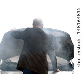 Auto driver standing in front of a broken down car open engine compartment hood with smoke from an automotive fire or hose leak steam waiting for emergency repair on a road