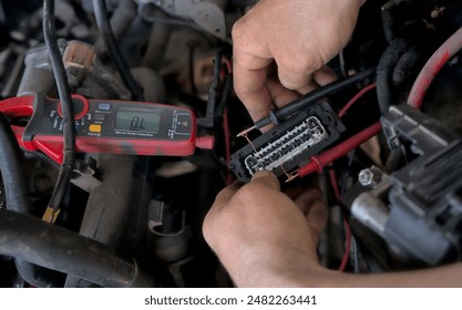 An auto electrician using a measuring device to check the voltage in a vehicle's electrical circuit, diagnosing wiring issues for repair. Auto service.