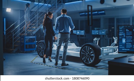 Auto Industry Design Facility: Male Chief Engineer Shows Car Prototype To Female Car Designer. Electric Vehicle Platform Chassis Concept Has Wheels, Engine And Battery. Screens Show 3D Cad Software