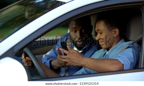 Auto instructor scolding young driver chatting\
smartphone lesson, safety\
rules
