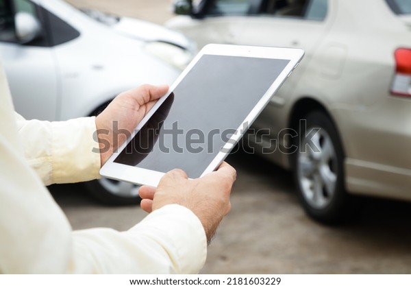 Auto insurance concept. A man, a company officer\
holding a tablet, takes pictures and records the accident car to\
inform the insurance\
company.