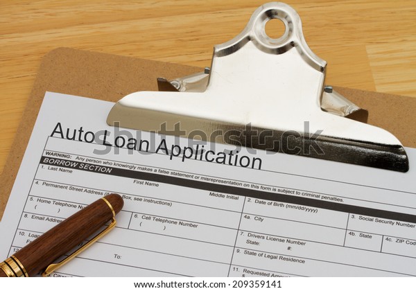 Auto Loan Application Form on a clipboard with a pen\
on a wooden desk