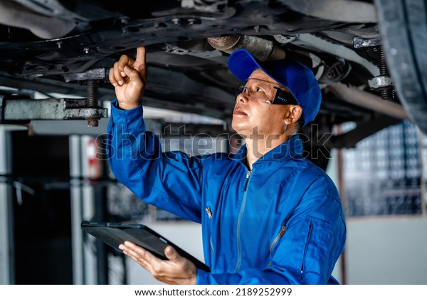 Auto mature mechanic repairman in uniform using\
digital tablet checking auto suspension repair in the garage,\
change spare part, check the mileage of the car, checking and\
maintenance service\
concept.