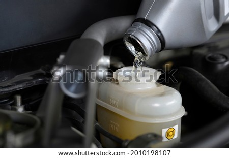 Auto mechanic adding brake fluid in brake fluid reservoir.