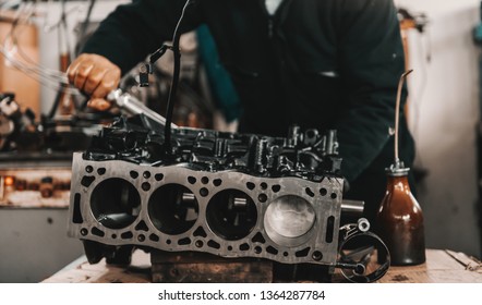 Auto mechanic adjusting cylinder head on engine block with wrench at workshop.