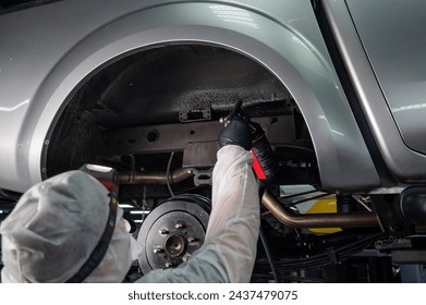 An auto mechanic applies anti-corrosion mastic to the underbody of a car. - Powered by Shutterstock