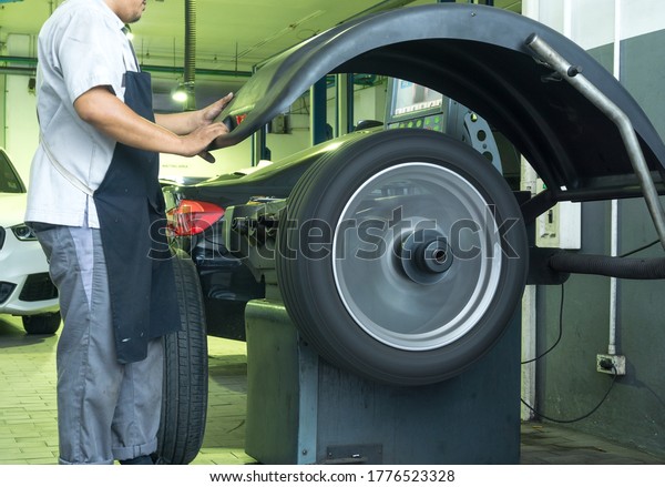 Auto mechanic balances the car wheel on\
the wheel balancer machine in the Car\
garage.