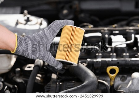 Auto mechanic changes oil filter for diesel cars, holds new oil filter in his hands against background engine compartment, close-up. Concept replacing auto parts, servicing car in car service center. 