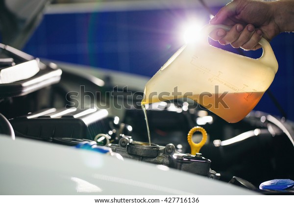 Auto mechanic is changing motor oil into a engine at\
car station. Close up