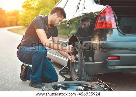 Auto mechanic changing  tire on car on road