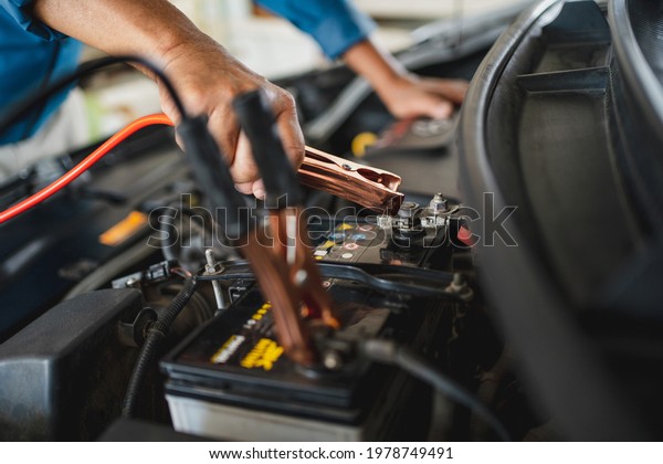 Auto mechanic is\
charging the battery. He works in a garage. Car repair service and\
car problems concept.