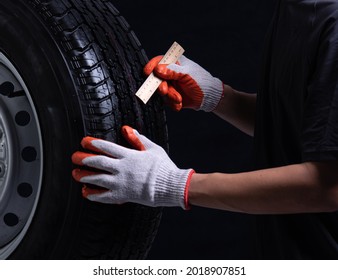 Auto mechanic checking a car tire on a black background,wood ruler measure the tread 