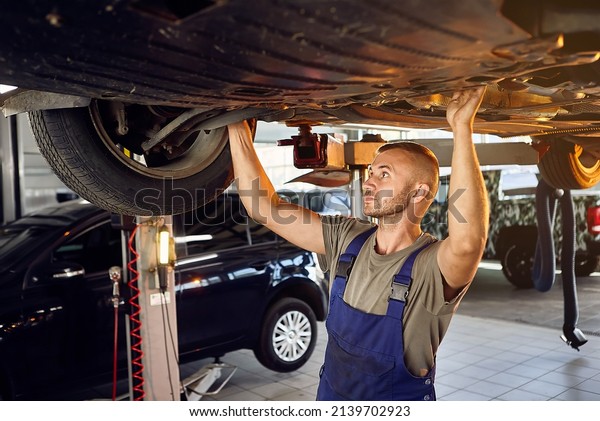 Auto mechanic checking running gear of automobile\
on service station. Male worker fixing problem with car. Vehicle\
maintenance concept