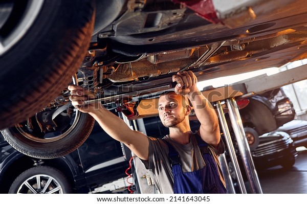 Auto mechanic checking running gear of automobile\
on service station. Male worker fixing problem with car. Vehicle\
maintenance concept