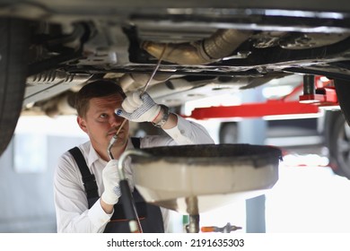 Auto Mechanic Checks Running Gear Of Car And Oil Leak At Service Station