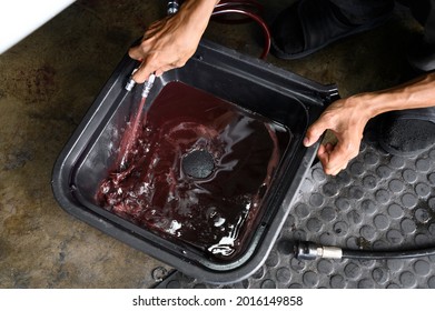 Auto Mechanic Draining Old Used Automatic Transmission Fluid Into The Oil Drain Pan.