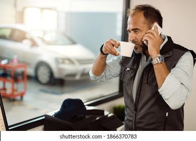 Auto mechanic drinking coffee while making a phone call at workshop's office. - Powered by Shutterstock