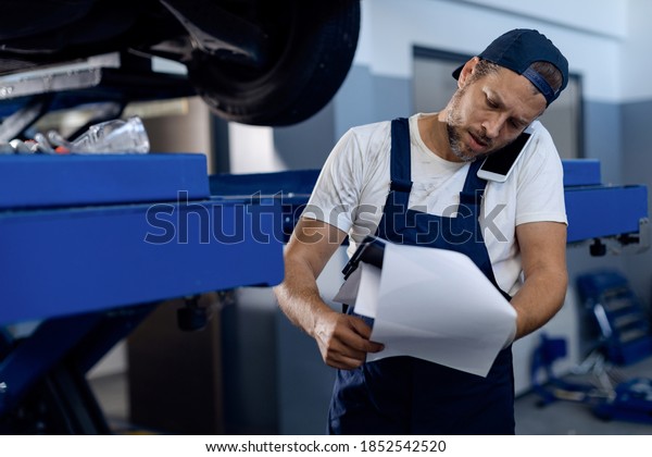 Auto mechanic examining paperwork and\
communicating over mobile phone in a repair\
shop.