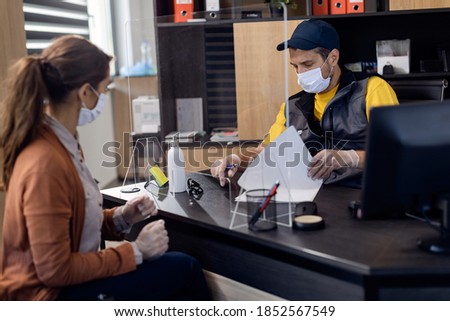 Auto mechanic examining paperwork while being with a customer in the office. They are wearing face masks due to coronavirus pandemic. 