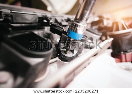 The auto mechanic is fastening the bolt of car ignition coil with the socket wrench to fix the vehicle ignition system, sunlight on background