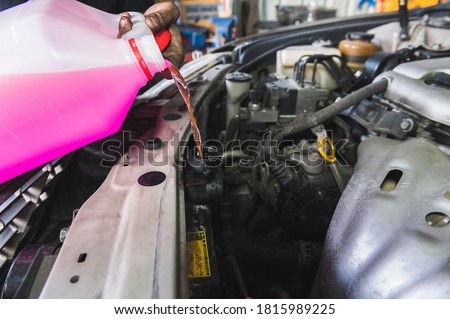 Auto mechanic filling Pre-mixed Super Long Life Coolant fluid in car radiator fill hole.