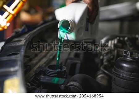 Auto mechanic filling super long life coolant fluids into car radiator fill hole.