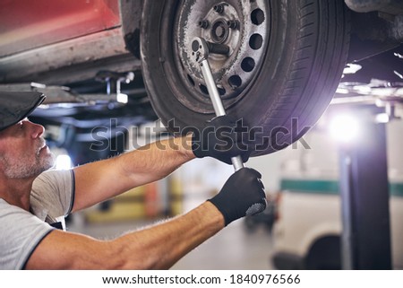 Auto mechanic in gloves tightening bolts on wheel with torque wrench while working in automobile repair garage