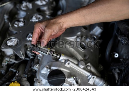 Auto mechanic hand installing variable valve timing solenoid on the engine.