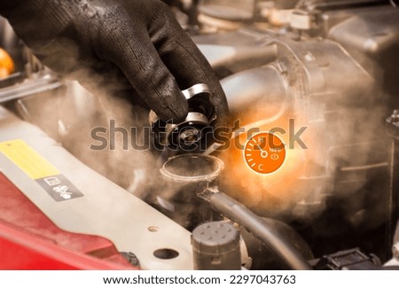 Auto mechanic hand opens the radiator cap with steam escaping around the engine compartment from the high heat,water temp gauge symbol with high temperature,Car maintenance service concept.