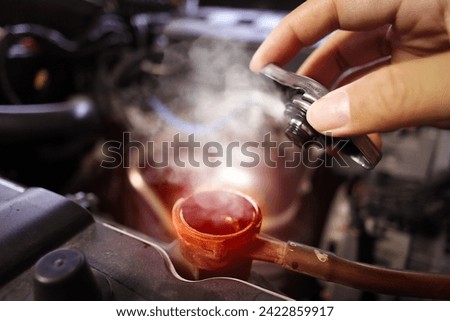 Auto mechanic hand opens the radiator cap with steam escaping around the engine compartment from the high heat , Car maintenance service concept.