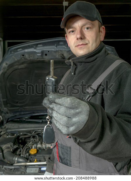 Auto mechanic holding a car key of\
the repaired car waiting to be handed over to the\
customer