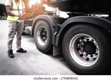 Auto Mechanic Holding Clipboard Is Checking The Truck Wheels Tires. Mechanic Repairman Auto Service Shop. Inspection Maintenance And Safety Program Of Semi Truck.