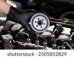 Auto mechanic holding fuel filter for diesel cars against background of engine compartment of car, close-up. Auto parts replacement, car maintenance. Checking filter condition before installation. 