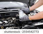 Auto mechanic holding fuel filter for diesel cars against background of car engine compartment. Man working intently under hood of vehicle to ensure it works properly. Car maintenance, repair services