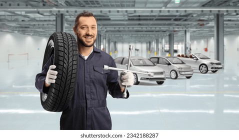 Auto mechanic holding a tire on his shoulder and a lug wrench inside a car garage - Powered by Shutterstock