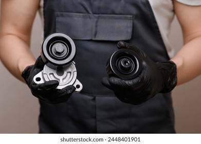 Auto mechanic holds in hands in black gloves tension roller with car serpentine belt tensioner and parasitic roller, close-up. Replacing auto parts, car maintenance, purchasing auto parts - Powered by Shutterstock