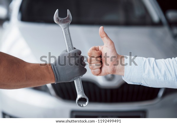 The auto mechanic holds the key\
in the client\'s hand and lifts his thumb up. Well done\
work.