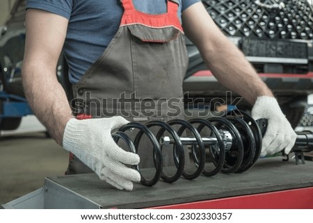 An auto mechanic holds a new shock absorber strut and a spring in his hands. The specialist evaluates the compatibility of the car suspension parts. Car maintenance.