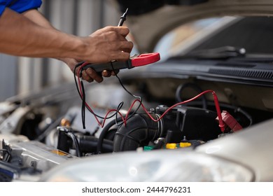 An auto mechanic is inspecting the electrical system and battery inside the car. - Powered by Shutterstock