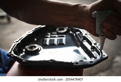 Auto Mechanic Installing An RTV Silicone Liquid Gasket On The Oil Pan Flange.