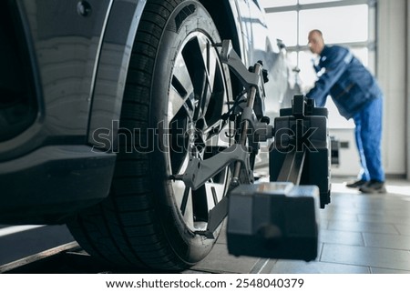 Auto mechanic installing sensor during suspension adjustment and automobile wheel alignment work at repair service station