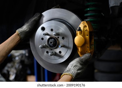 Auto mechanic installing two piston brake calipers and disc brake rotor.