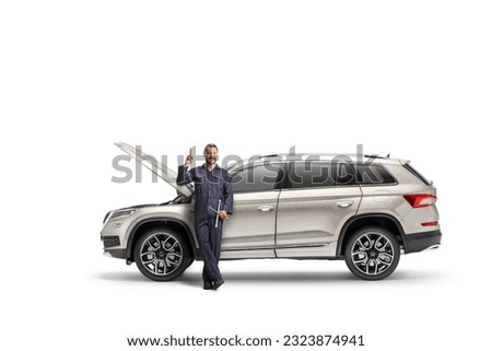 Auto mechanic leaning on a SUV with an open hood and pointing up isolated on white background 