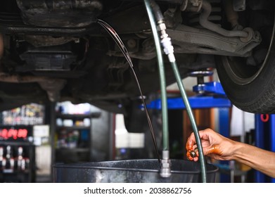 Auto mechanic loosen auto transmission oil drain plug and then let the old used transmission oil flow out of the oil pan flange. - Shutterstock ID 2038862756