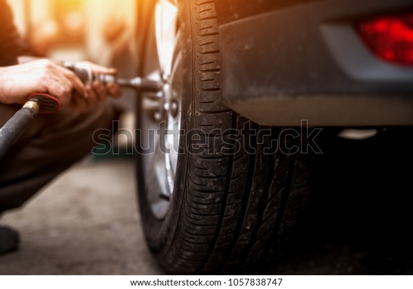 Auto mechanic man with electric screwdriver\
changing tire outside. Car service. Hands replace tires on wheels.\
Tire installation concept.