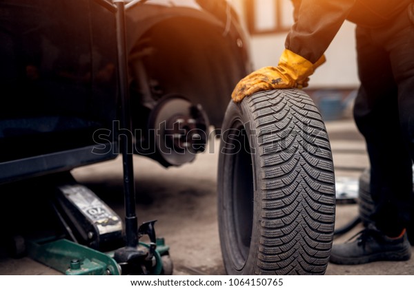 Auto mechanic man with electric screwdriver\
changing tire outside. Car service. Hands replace tires on wheels.\
Tire installation concept.